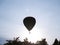 In silhouette hot air balloon drifts through atmosphere above treetops