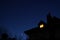 Silhouette of house roof with chimney and lit attic small window at night