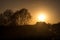 Silhouette of a house and trees near empty road with dust in countryside at sunset. Sunset colors. Clear sky.