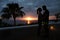 Silhouette of a hugging couple and palm tree with sunset over the sea