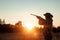 Silhouette of a hunter in a cowboy hat with a gun in his hands on a background of a beautiful sunset. The hunting period, the fall