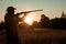 Silhouette of a hunter in a cowboy hat with a gun in his hands on a background of a beautiful sunset. The hunting period, the fall