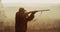 Silhouette of hunter in gold sunset light find the target and aims with the rifle foggy landscape on background