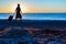 Silhouette of Lady walking along Sea Surf pulling Travel Suitcase