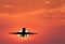 Silhouette of landing aircraft and red sky with sun