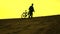 Silhouette of lonely biker walking with his bike along sand dune, yellow sunset colors. 4K video