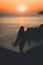 Silhouette of a lonely female holding a surfing board walking by the sea at sunset