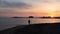 Silhouette of lonely man with fishing rod standing on empty beach with pink sunset on horizon. Silhouette of man fishing on sunset
