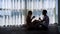 Silhouette of loving couple sitting on floor and drinking morning coffee