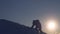 Silhouette of male climber climbing to top of snowy mountain in glare of setting sun in winter. Traveler in snowy