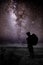 Silhouette of man with backpack and trekking poles against amazing Milky Way at night. Photographer and star in the night sky.