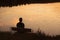 Silhouette of man on bench in golden sunset by lake.