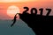 Silhouette Man climbs into cliff to the goal setting of word Happy New Year 2017 with sunset in background.