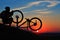 Silhouette of man cyclist repairing a bike against sunset