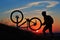 Silhouette of man cyclist repairing a bike against sunset