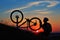 Silhouette of man cyclist repairing a bike against sunset