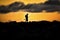 Silhouette of man with fishing poles walking across rocks of jetty at sunset