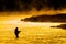 Silhouette of Man Flyfishing Fishing in River Golden Sunlight