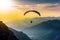 Silhouette of a man flying on a paraglider against the backdrop of a sunset over high mountains. Generative ai