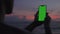 Silhouette man holds vertical mobile phone one hand and swiping touch screen. Use green screen for copy space closeup