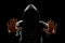 Silhouette of a man in a hood on a black background, the face is not visible, shows the palms in the camera. The concept of a