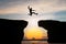 Silhouette of Man jump through the gap between hill on sunset background, business concept idea