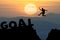 Silhouette man jumps to the word GOAL with sunrise.