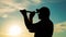 A silhouette of a man looking at using a monocular telescope against a dramatic sky at sunset. business idea concept, look to the