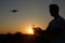 Silhouette of a man piloting drone in the air with a remote controller in his hands on sunset. Pilot takes aerial photos