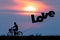 Silhouette of man ride on bicycle with air balloons for wording LOVE at sunset sky (Love valentine concept)