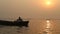 Silhouette of man rowing down the Ganges at sunset, with birds above water.