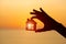 Silhouette of man`s hand holding small wooden house against sunset or sunrise light