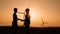 Silhouette man shaking hands with engineer with wind turbines on background. Two colleagues making deal about successful