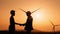 Silhouette man shaking hands with indian engineer with wind turbines on background. Two colleagues making deal about