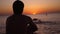 Silhouette of a man sitting alone on the beach looks sunset. Lonely, thinking person.