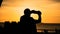 Silhouette of man standing on beach taking selfie photo during sunset