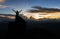 Silhouette man standing on giant rock and spreading hand on mountain top at sunset
