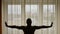 Silhouette of man standing and stretching in front of orange yellow curtains window morning indoors city.