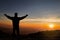 Silhouette of man standing on top of mountain with hands raised up on sunrise background, successful, achievement and winning