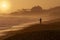 Silhouette of a man surf fishing at sunset at the waters edge with the San Onofre nuclear power plant in the background