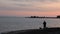 Silhouette of man throwing fishing rod in sea at pink sunset. Fisherman fishing on seashore at sundown