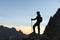 Silhouette of a man traveler in a cap with a backpack and trekking poles. Stands on the edge of a cliff against the
