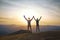 Silhouette of man and woman standing on edge of mountain and holding hands up on sunset sky and mountains background.