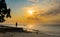 Silhouette of Masai standing on the beach with traditional weapon and a wooden Dhow boat in the water, sunset, Zanzibar