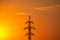 Silhouette of a mast of a high-voltage power line in a sunset. Steel metal pylon on orange background of the setting sun. Power