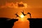 Silhouette of Men are jumped between high cliff at sunset