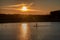 Silhouette of men on sup board with oar in hands on lake in evening with magnificent sunset in background