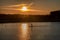 Silhouette of men on sup board with oar in hands on lake in evening with magnificent sunset in background