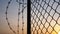 Silhouette of mesh fence and barbed wire with dark sky at sunset