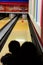 A silhouette of a mother and child watching a ball go down a bowling alley.
